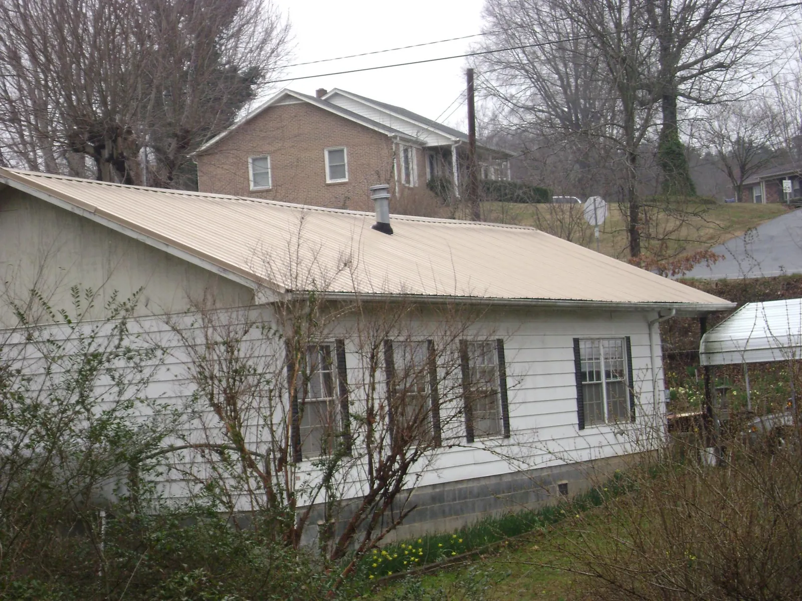 Tan metal roof on a white sided house set into a hillside — Commercial Roofing by Roofing Brothers in Moore Haven