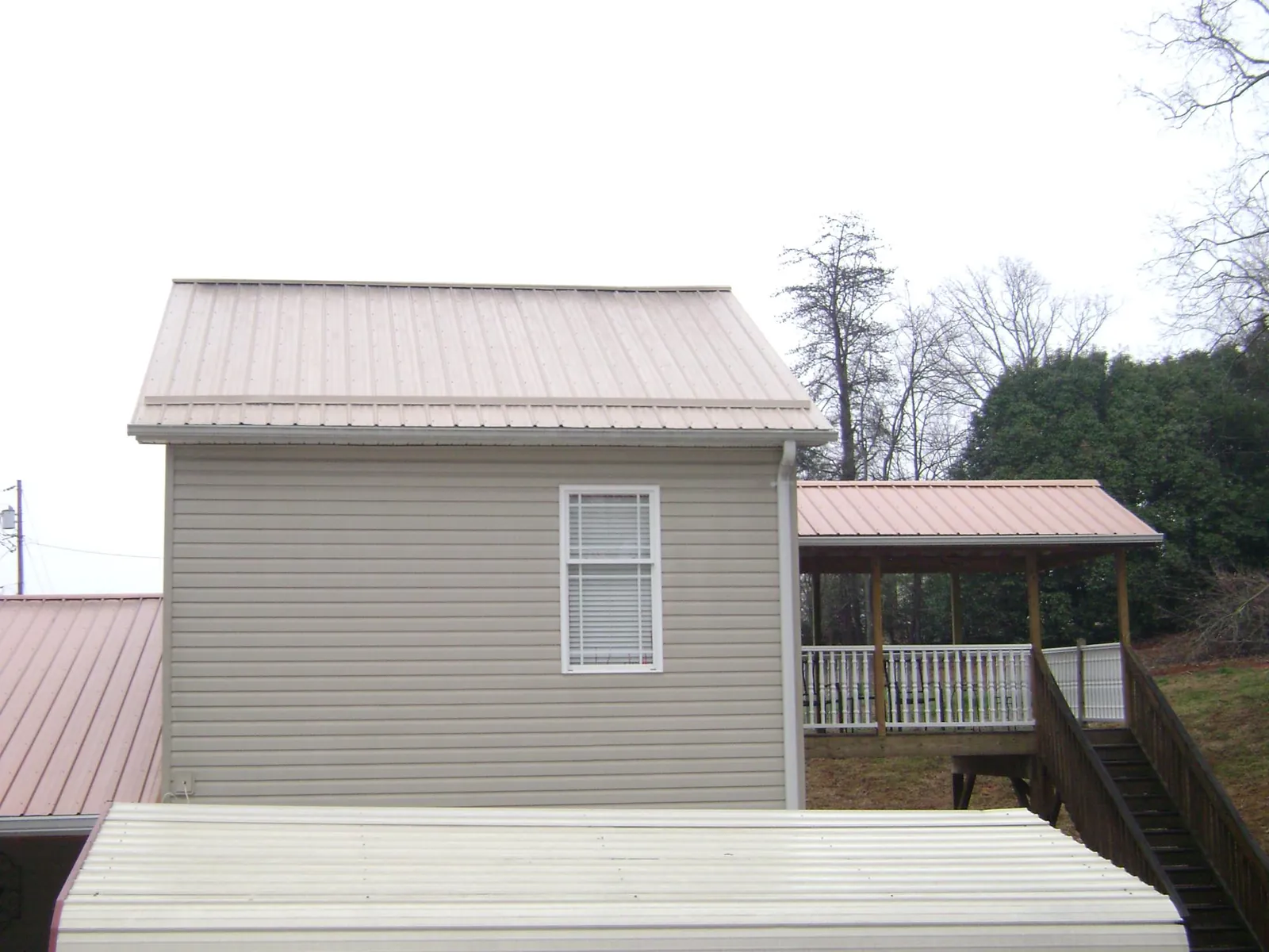 Tan metal roofs on a two story addition and attached porch, from a Roof Replacement job in Moore Haven